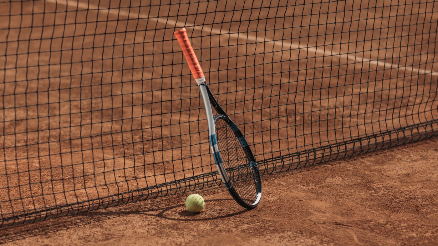 tennis ball and racket leaning on net